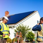 A sunny suburban backyard, with a two-story home taking center stage. On the roof, a meticulously installed MSM Solar LLC solar panel system, its sleek black panels contrasting beautifully against the white siding. In the foreground, a professional solar technician in a safety vest inspects the wiring, ensuring optimal performance. The middle ground features a well-organized worksite, with tools and equipment neatly arranged. The background showcases a clear blue sky, accentuating the renewable energy narrative. Warm, natural lighting bathes the scene, conveying a sense of efficiency and environmental responsibility.