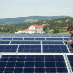 A sprawling solar power system stands against a clear sky, with sleek black panels arranged in neat rows. In the foreground, a technician from MSM Solar LLC examines the connections, ensuring optimal efficiency. The middle ground features a mix of modern and traditional architecture, hinting at the integration of renewable energy into the built environment. In the background, rolling hills and lush greenery create a serene, natural backdrop, emphasizing the harmony between technology and the environment. Soft, directional lighting casts subtle shadows, conveying a sense of thoughtful design and careful engineering.