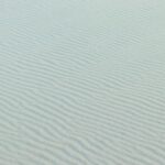 Fine rippled sand pattern under a bright sky, capturing the essence of a tranquil desert scene.