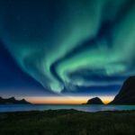 Breathtaking view of the Northern Lights illuminating the Lofoten Islands in Norway at twilight.