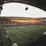 Wide-angle view of a lively soccer match in an Iraqi stadium, showcasing vibrant atmosphere and architectural details.