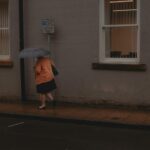 A woman with an umbrella walking along a rain-soaked street in Leeds, UK.