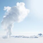 Snow-covered Icelandic landscape featuring geothermal steam plume against clear sky.