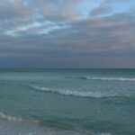 A serene view of gentle waves and a tranquil sea under a cloudy sky at Destin Beach, Florida.