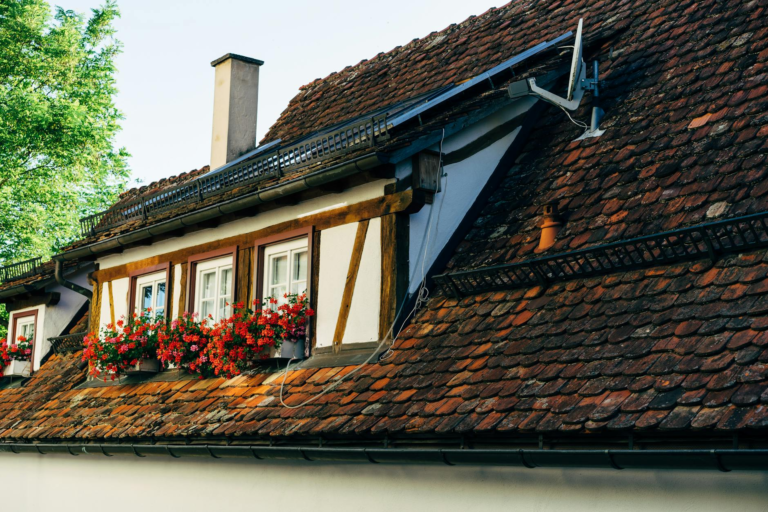 Close-up of a quaint house with a red brick roof, solar panels, and flower boxes.