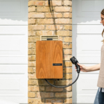 A woman uses a home electric vehicle charger mounted on a brick wall.