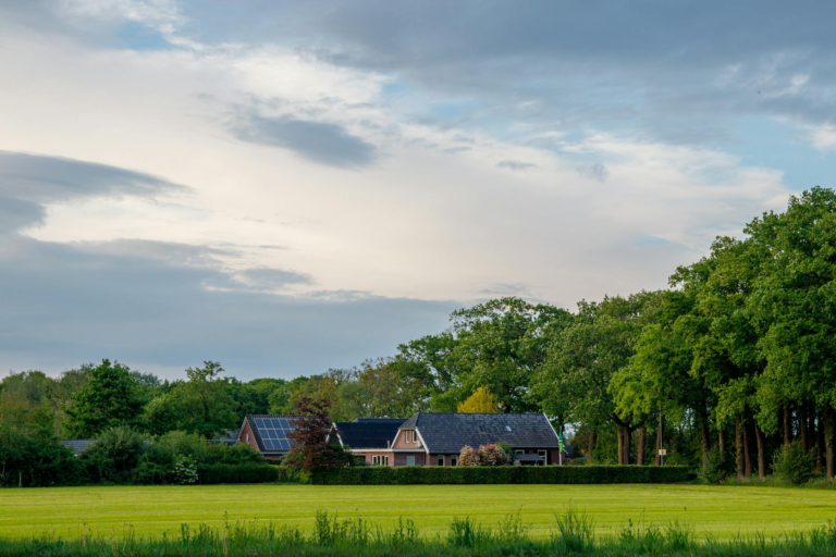 Charming rural home with solar panels in a lush green landscape under a cloudy sky.