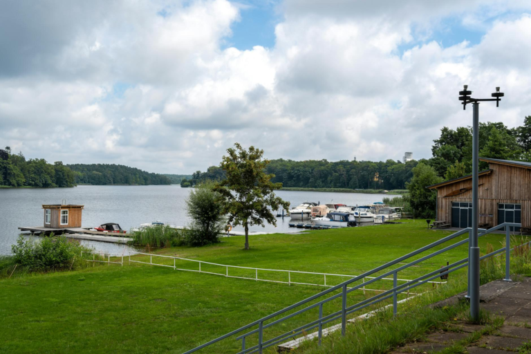 Idyllic view of a tranquil lake with docks, boats, and lush greenery under a cloudy sky.