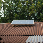 Solar panel on a rusty corrugated roof with green foliage background, symbolizing sustainable energy.