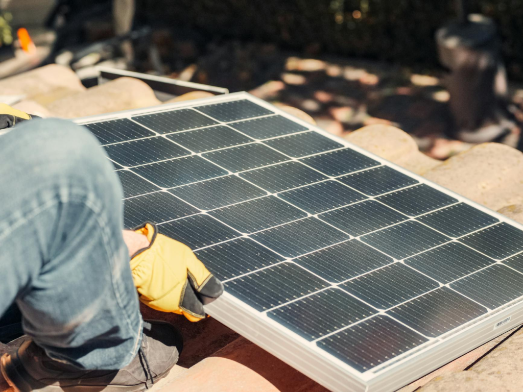 A worker installs a solar panel on a sunlit rooftop, exemplifying renewable energy.