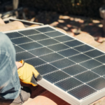 A worker installs a solar panel on a sunlit rooftop, exemplifying renewable energy.