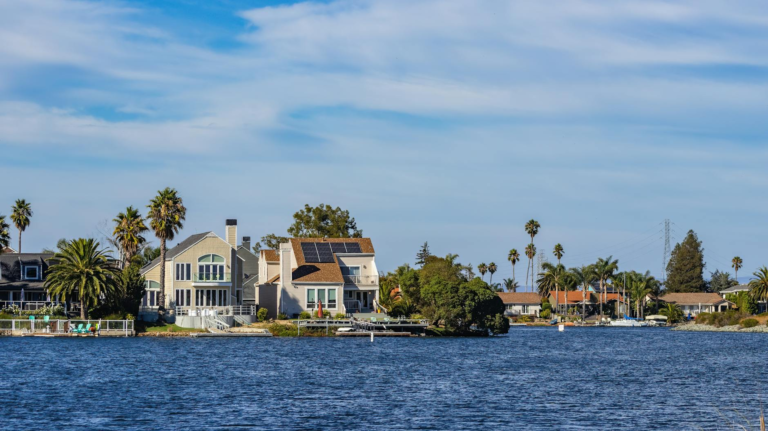 Charming waterfront homes with palm trees and solar panels reflecting in blue water.