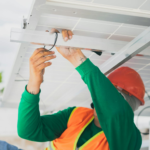 A solar technician in PPE installs a solar panel, showcasing renewable energy work.