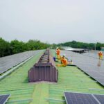 Team installing solar panels on a large rooftop under a clear sky, promoting renewable energy.