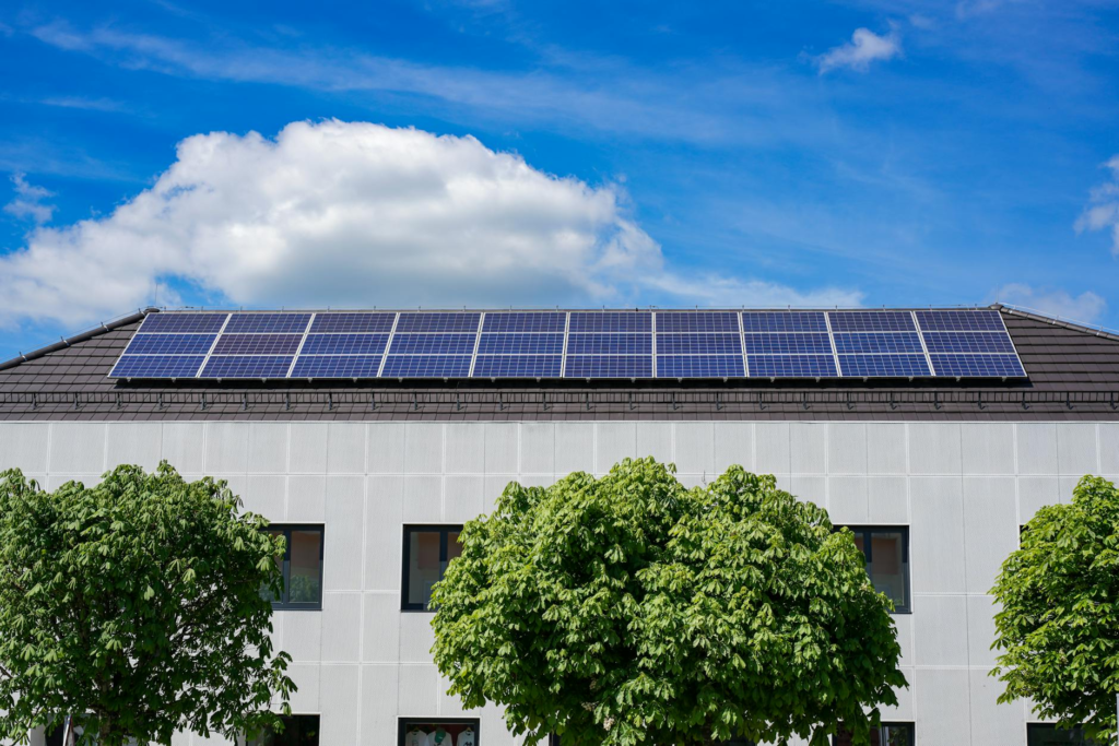 Energy-efficient building topped with solar panels and surrounded by lush trees.