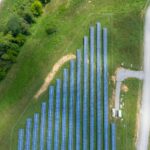 Aerial view showing a solar panel array in a lush rural landscape with a road.