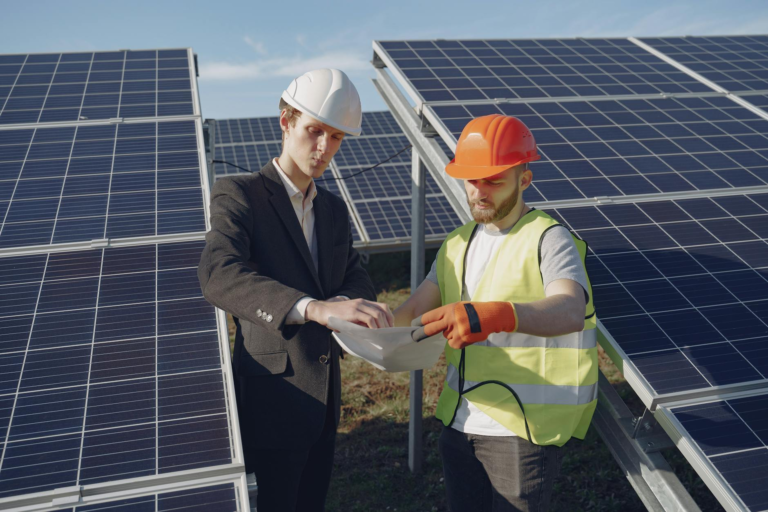 Two engineers inspecting solar panels at a renewable energy site under clear blue skies.