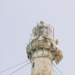 A close-up view of an old lighthouse tower featuring solar panels against a clear sky.