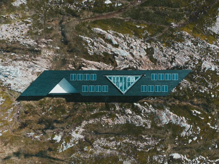 Modern house with solar panels on rugged landscape, seen from above.