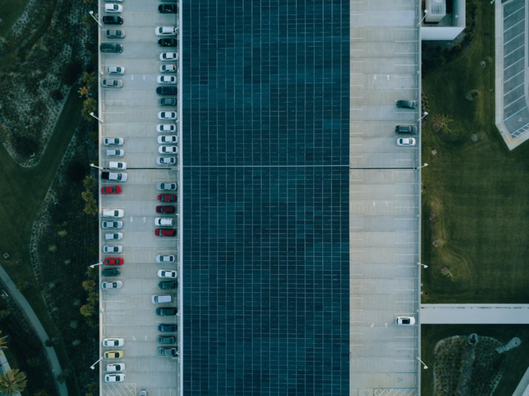 Top view of a parking lot with cars and solar panels, showcasing urban sustainability.