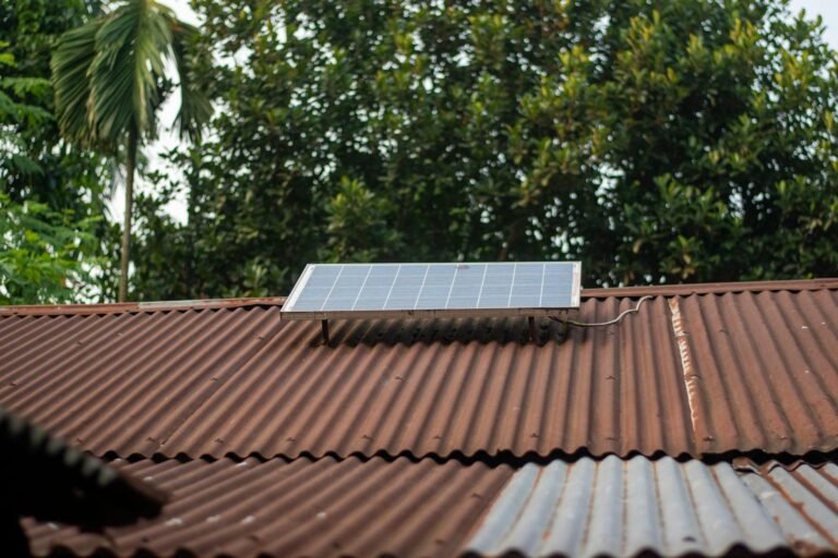 Solar panel on a rusty corrugated roof with green foliage background, symbolizing sustainable energy.