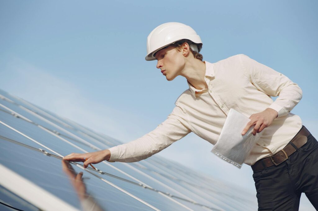 A solar technician in a hard hat inspecting photovoltaic panels under clear skies.