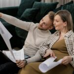A couple sitting on a sofa reviewing architectural blueprints, symbolizing home buying or renovation.
