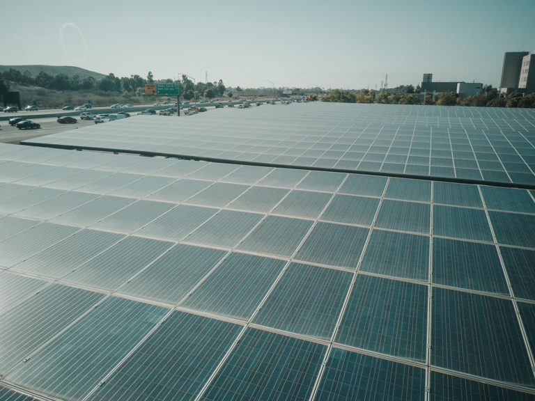 Rows of solar panels near a highway capture renewable energy under a clear sky.