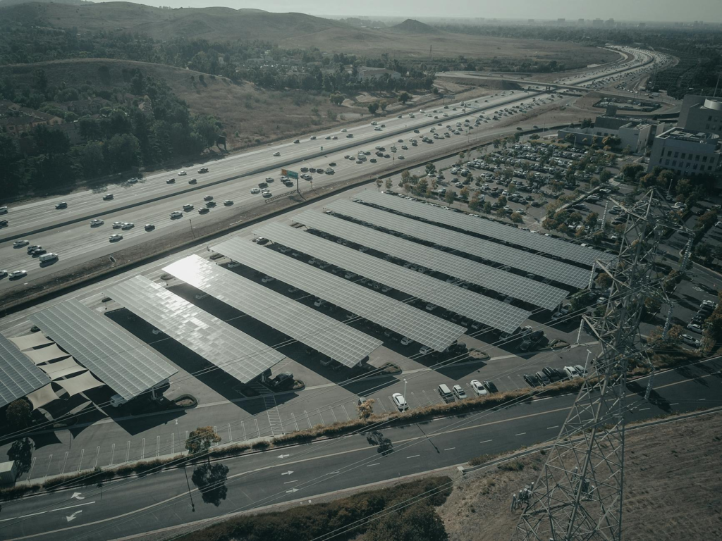 Aerial photo of a solar farm beside a busy highway with cars and power lines.