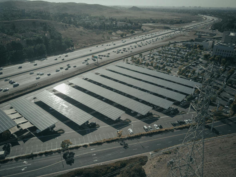 Aerial photo of a solar farm beside a busy highway with cars and power lines.