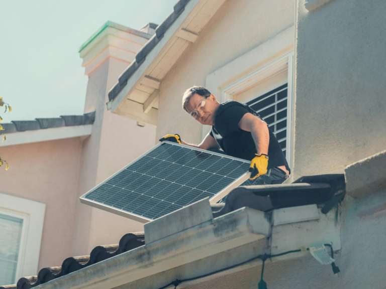 A technician in protective gear installs solar panels on a house roof, promoting sustainability.