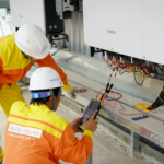 Two electrical engineers installing and testing solar power systems wearing safety gear at a construction site.