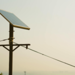A single solar panel mounted on a tall post against a clear sky, symbolizing renewable energy.