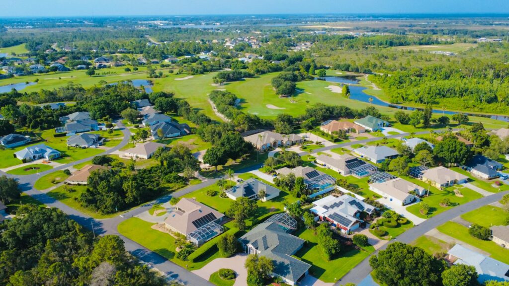 Aerial view of a sunny suburban neighborhood with green landscapes and solar-powered homes.