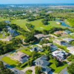 Aerial view of a sunny suburban neighborhood with green landscapes and solar-powered homes.