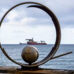 Artistic coastal sculpture frames a distant vessel on a serene ocean backdrop.