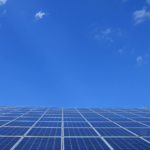 A low angle view of solar panels under a bright blue sky with clouds.