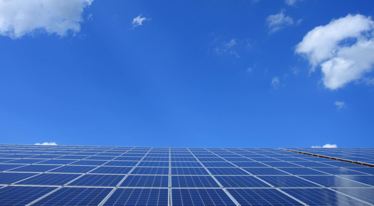 A low angle view of solar panels under a bright blue sky with clouds.