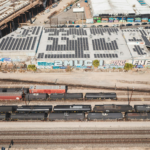 Aerial view of railroad tracks beside urban buildings with graffiti and solar panels.