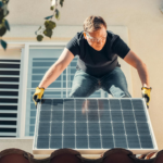 A man in safety glasses installs a solar panel on a house roof, promoting renewable energy.