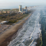 Drone shot of South Padre Island beach with waves and buildings along the coast.
