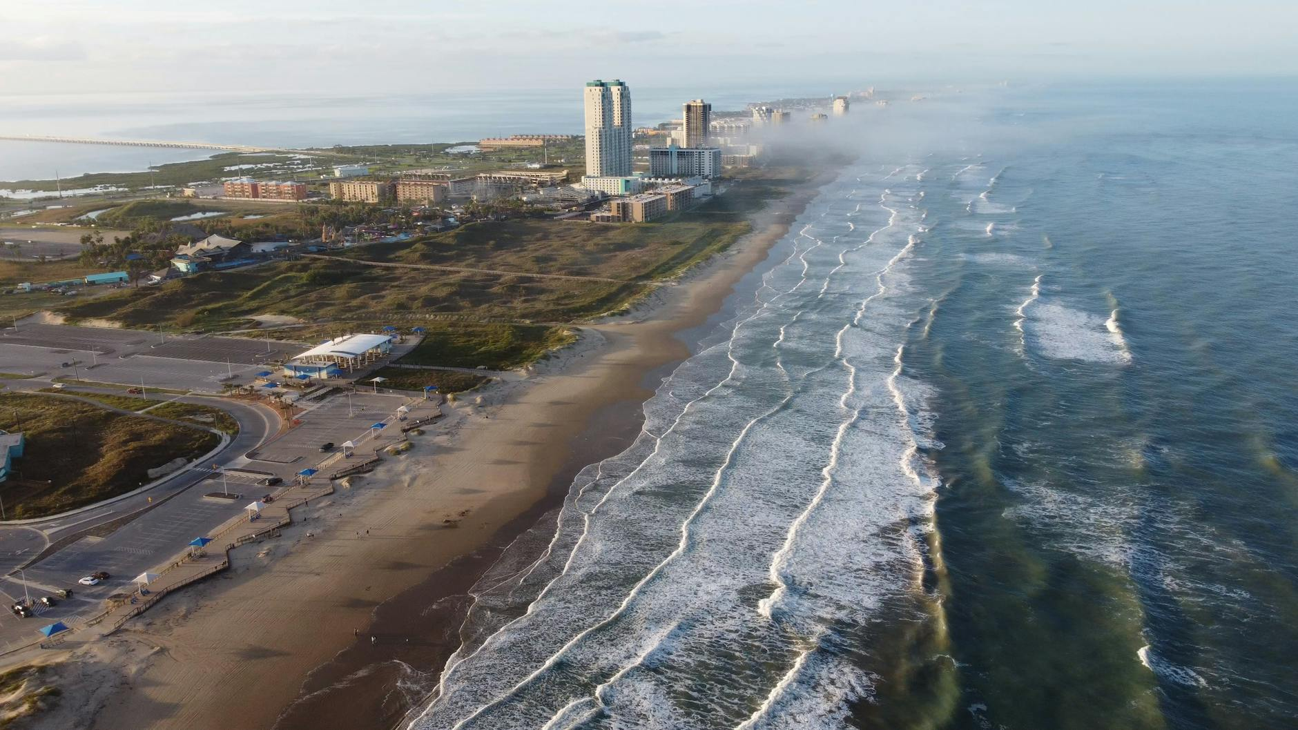 Drone shot of South Padre Island beach with waves and buildings along the coast.