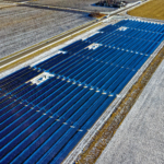 Aerial shot of expansive solar panel installation in snowy fields during daylight in Claremont, MN.