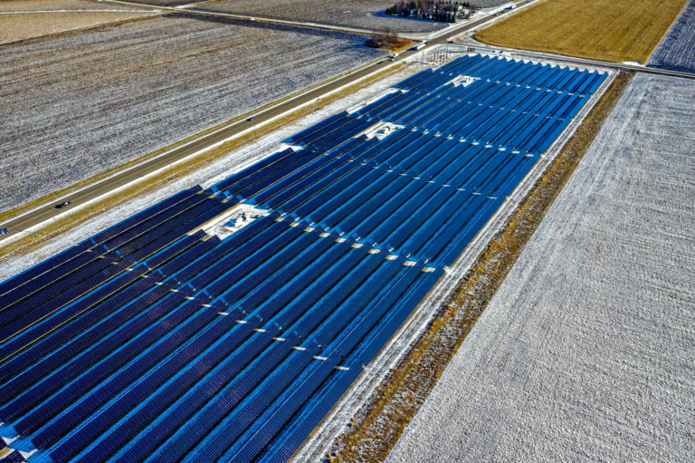 Aerial shot of expansive solar panel installation in snowy fields during daylight in Claremont, MN.