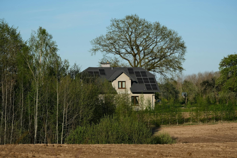 Modern house with solar panels surrounded by lush trees and fields, embracing sustainable living.
