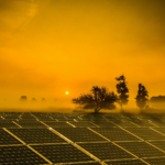 A vibrant sunrise over solar panels in a misty field, showcasing renewable energy.