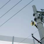 Utility pole with electrical wires and equipment against a clear blue sky, showcasing urban infrastructure.