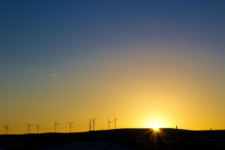 Silhouette of wind turbines against a vibrant sunset sky, capturing renewable energy theme.