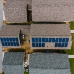 Top-down view of suburban houses featuring solar panels on roofs, showcasing renewable energy use.