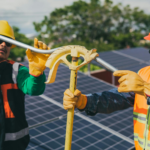 Two construction workers assembling solar panel equipment under sunny conditions, showcasing teamwork and renewable energy.